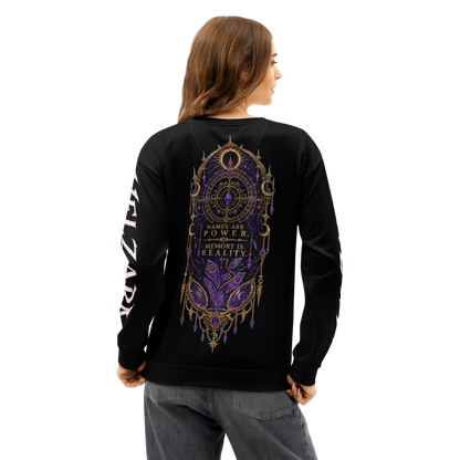 A woman shown from the back wearing a black crewneck sweatshirt with a large purple and gold mandala-style graphic on the back and white text down one sleeve, paired with gray jeans against a plain white background.